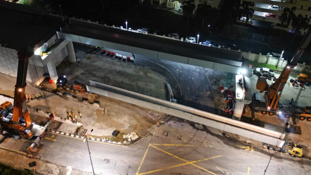 Night-time erection of a precast UHPC bridge girder is carried out using two mobile cranes in a synchronized tandem lift. The girder is hoisted, aligned, and positioned for seating onto the bridge