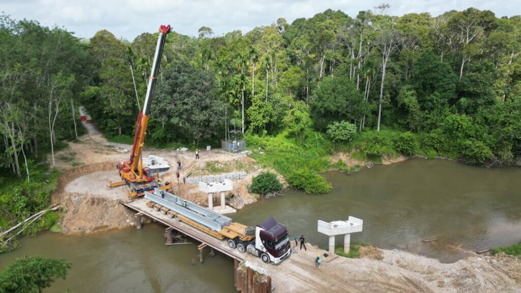 The girders are transported to site using a heavy haulage trailer and are being prepared for lifting operations by a mobile crane.