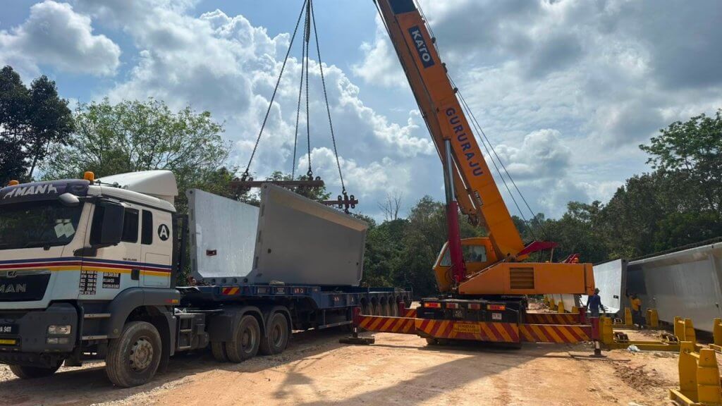Precast beam segments are being offloaded from delivery vehicles.
