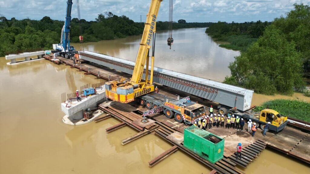 Beam launching activities are in progress. UBG2500 is being lifted using heavy mobile cranes from the temporary launching platform and positioned onto the permanent bridge bearings.