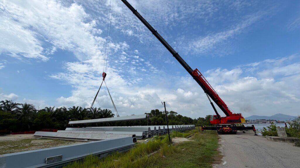 UHPFRC prestressed sheet piles are being lifted by mobile crane and transferred from the designated staging area onto a barge.